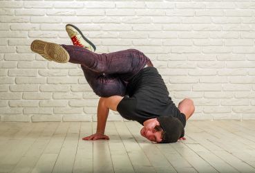 Ein junger Mann mit schwarzer Mütze in einer Breakdance-Pose am Boden.